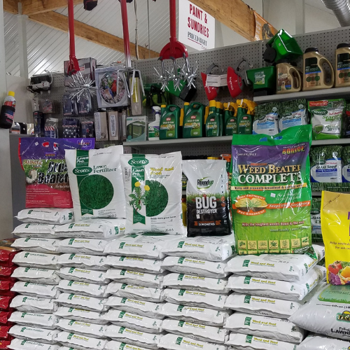 Bags of lawn care products are stacked in rows, including fertilizers and weed control. Shelves above hold gardening supplies. The setting is organized and colorful.