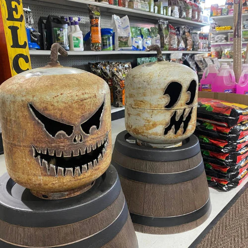 Decorative propane tanks with Halloween-themed faces; one resembles a sinister grin, the other a ghostly look, set in a store with gardening supplies.