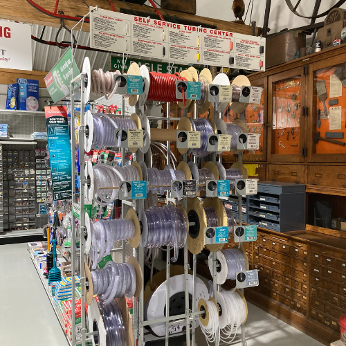 Display of assorted tubing and wires on spools in a hardware store aisle. Wooden cabinets line the back wall, contributing to a practical, organized vibe.