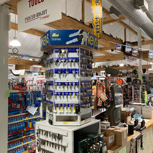 A hardware store with a key-cutting station in the foreground, surrounded by tools and gadgets. The atmosphere is busy and organized.