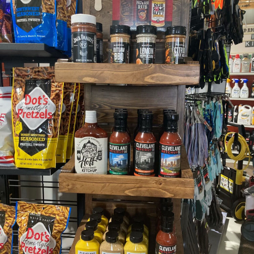 Wooden shelves in a store display bottles of Cleveland barbeque sauce, Jack Daniel's spices, hot ketchup, and mustard. Adjacent are Dot's Pretzels bags.