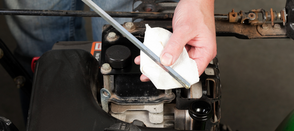 Hand wiping a dipstick to check oil level in a small engine.