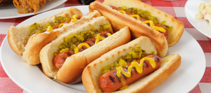 A plate of grilled hot dogs in buns with mustard and relish on them