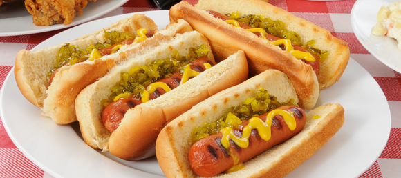 A plate of grilled hot dogs in buns with mustard and relish on them